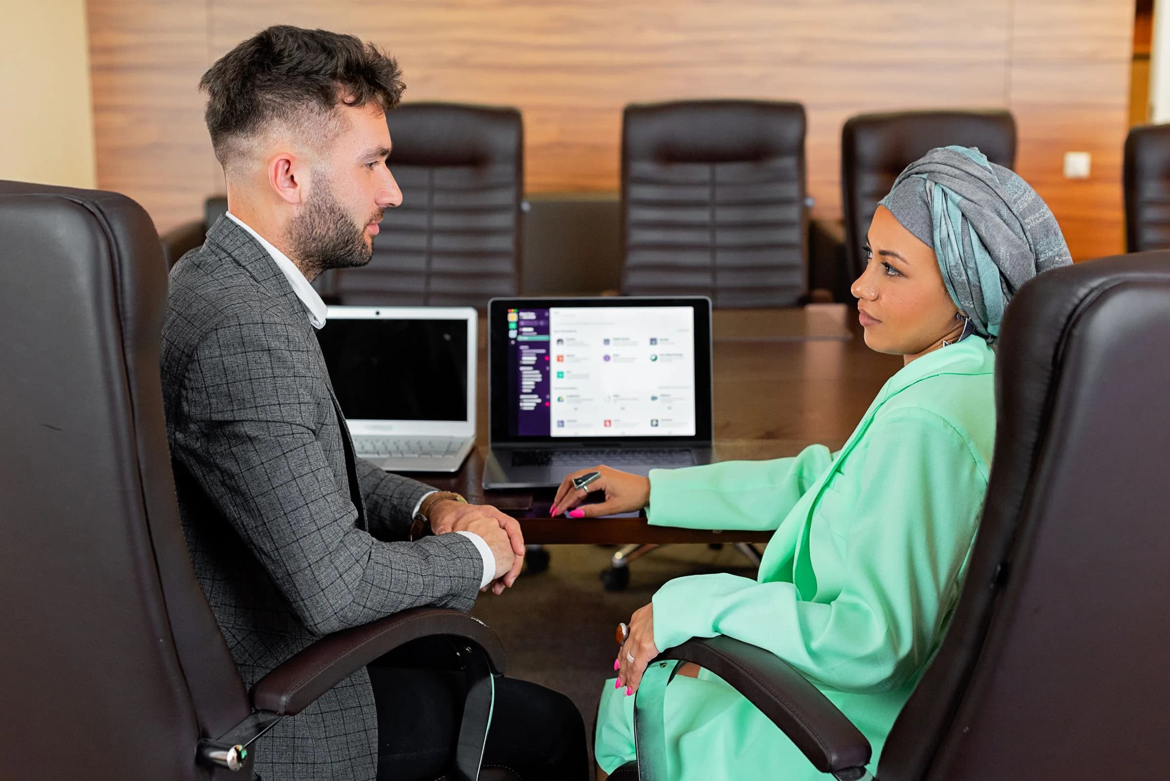 Two professionals discussing work with laptops in a meeting room