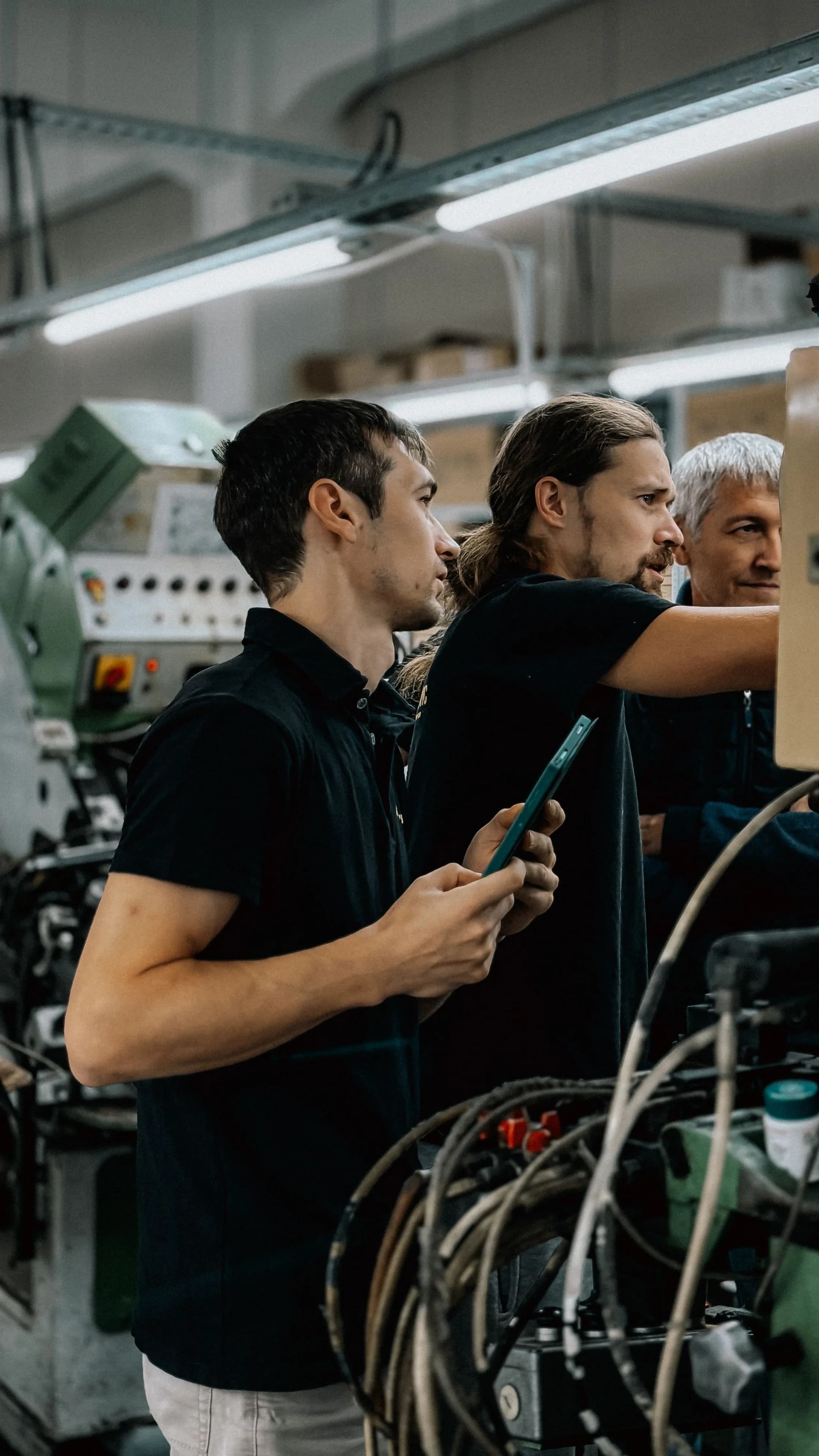 Three colleagues inspecting machinery in a manufacturing workshop